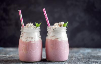 Fotografia de dois recipientes decorativos de vidro com frapê com Leite MOÇA, guaraná e suco de limão. No mesmo copo tem um canudo rosa e branco e hortelã. Fotografia de dois recipientes decorativos de vidro com frapê com Leite MOÇA, guaraná e suco de limão. No mesmo copo tem um canudo rosa e branco e hortelã.