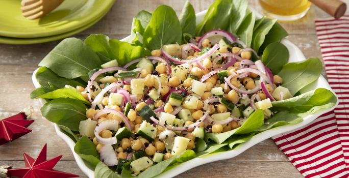 Foto em tons vivos da receita de salada de grão de bico e batata doce servida em um prato grande retangular de porcelana branca sobre uma mesa de madeira com um paninho listrado vermelho ao lado