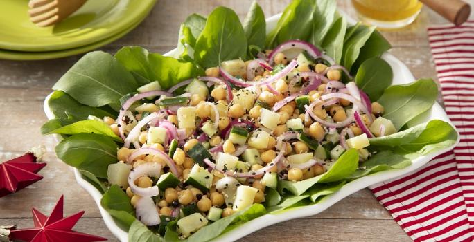 Foto em tons vivos da receita de salada de grão de bico e batata doce servida em um prato grande retangular de porcelana branca sobre uma mesa de madeira com um paninho listrado vermelho ao lado