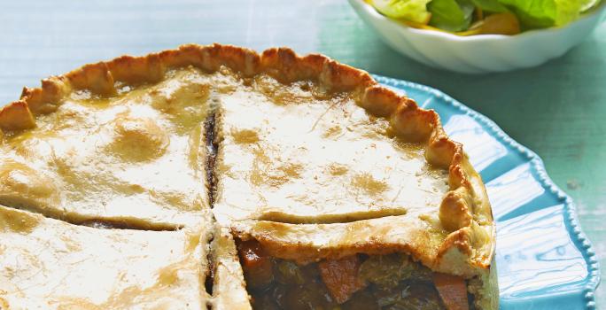 em um prato redondo e azul contém uma torta com uma fatia retirada e ao lado um pote branco e redondo com folhas.