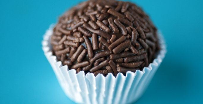 Fotografia de um brigadeiro em uma forminha sobre uma mesa azul.