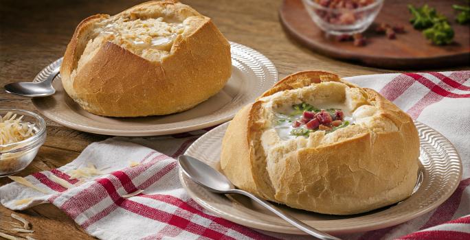 Foto de um pão italiano com sopa creme de queijo dentro e bacon decorando em cima da receita