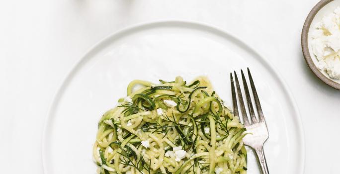 Fotografia em tons claros vista de cima de um macarrão com molho de sálvia, manteiga e vinho, com um garfo ao lado, dentro de um prato branco raso. Ao redor, outro prato com a mesma massa, e, um recipiente pequeno e fundo com molho branco cremoso.