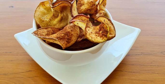 Foto da receita de Chips de Maçã. Observa-se um potinho branco de porcelana com os chips dentro polvilhados de canela.
