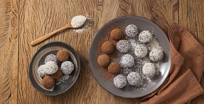 fotografia em tons de marrom e branco de uma bancada marrom vista de cima, contém dois pratos redondos cinza e ambos contém trufas com aveia por cima e chocolate