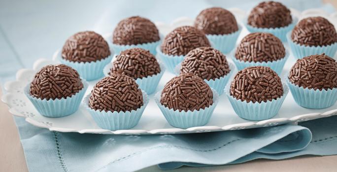 Foto de um prato branco que está em cima de um pano azul com vários brigadeiros dentro de forminhas azuis