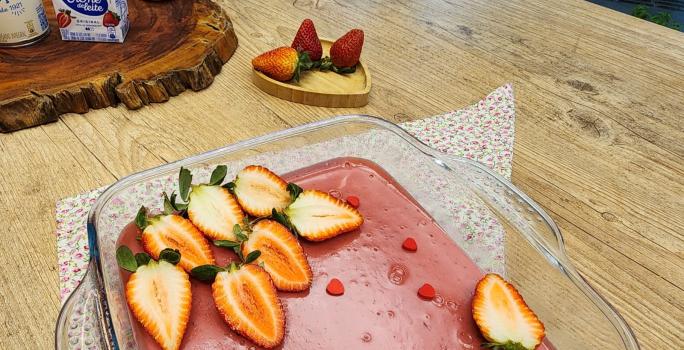 Foto da receita de Doce amor de morango. Observa-se uma travessa com o creme rosa e morangos frescos decorando.