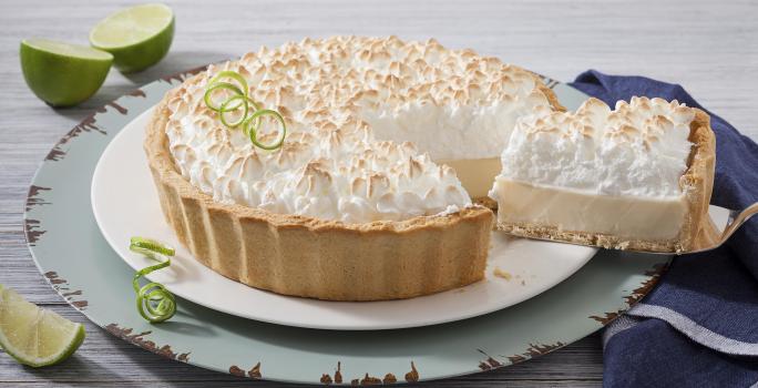 Foto de uma torta de limão em cima de um prato branco e com uma fatia generosa sendo retirada