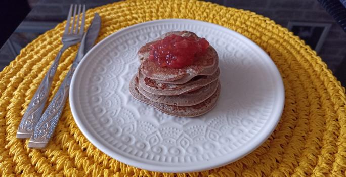 Imagem da receita de Panqueca de batata doce sem glúten com cobertura de geleia de frutas, em um prato branco, sobre uma mesa e ao lado os talheres