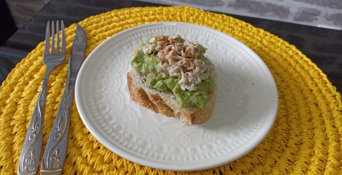 Imagem da receita de Avocado Toast, em um prato branco, sobre uma mesa e ao lado os talheres