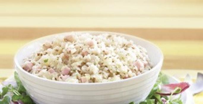 Fotografia em tons de amarelo em uma bancada de madeira clara, um pano amarelo, um prato redondo com salada de alface e cebola roxa e um potinho branco com a salada de arroz dentro dele.