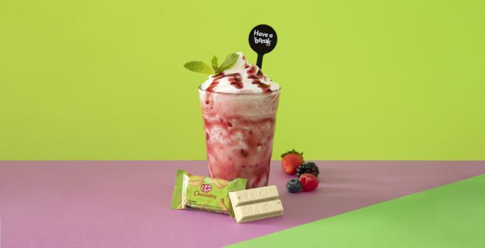 Foto em tons de cor de rosa e verde da receita de smoothie iogurte servida em um copo alto sobre uma mesa cor de rosa com um kit kat hortelã à frente