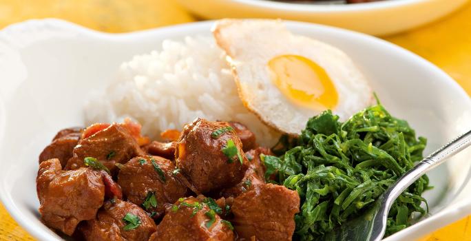 fotografia vista de frente, contém dois recipiente branco e redondo e ambos contém: arroz, couve, pedaços de carne e ovo com um garfo para servir