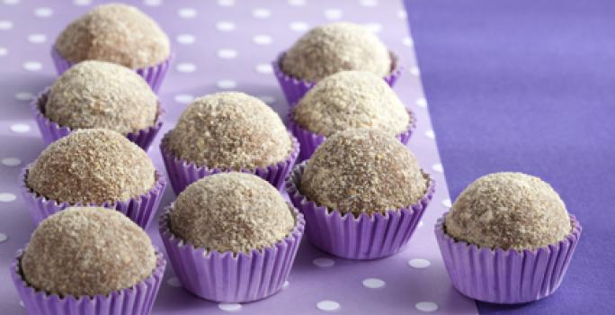 Fotografia em tons de roxo em uma mesa com uma toalha roxa escura, um paninho lilás com bolinhas brancas e vários brigadeiros de cookie dentro de forminhas de docinhos roxa.