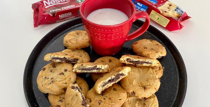 Fotografia de um prato preto servido de cookies e uma xícara vermelha com leite dentro.