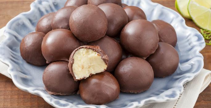 Fotografia em tons de marrom e azul de uma bancada de marrom com um paninho branco, sobre ele um prato azul com trufas. Ao fundo fatias de limão.