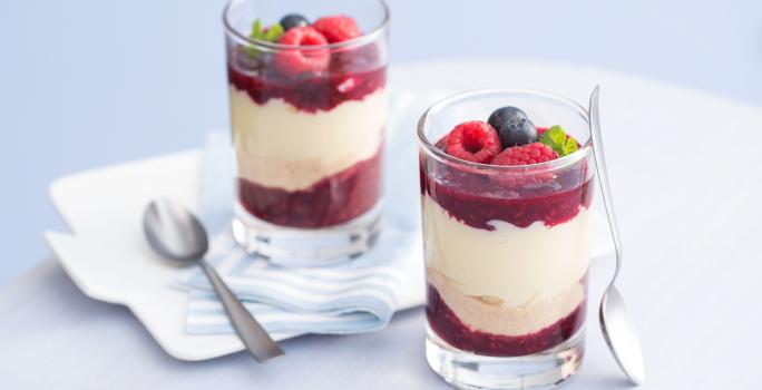 fotografia em tons de branco e vermelho tirada de dois copos transparentes com geleia de frutas vermelhas e leite MOÇA de colher com frutas vermelhas por cima e colheres ao lado.