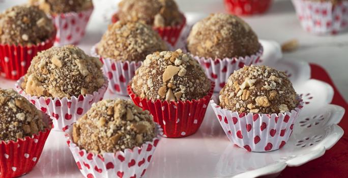 Fotografia em tons de vermelho em uma mesa vermelha com um prato redondo branco com os brigadeiros Classica de palha italiana colocados nele em forminhas de papel brancas e vermelhas com coraçãozinho.