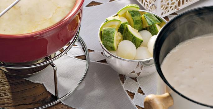 recipientes nas cores vermelho e branco ambos comporta o fondue de queijo, outros recipientes estão com os acompanhamentos para o fondue como pão, presunto entre outros.