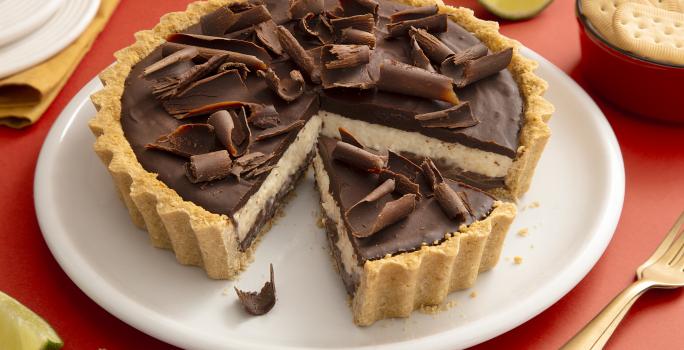 Foto da receita de Torta de Limão com Chocolate. Observa-se uma torta com cobertura de ganache e raspas de chocolate com um pedaço fatiado.