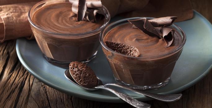 Foto de duas pequenas tigelas com mousse de chocolate dentro em cima de um prato azul