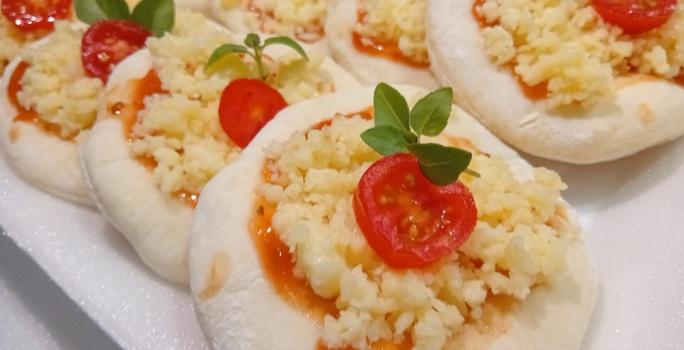 Foto da receita de Mini Pizza. Observa-se os discos pequenos um ao lado do outro, recheados com molho de tomate, queijo, tomate cereja e manjericão.