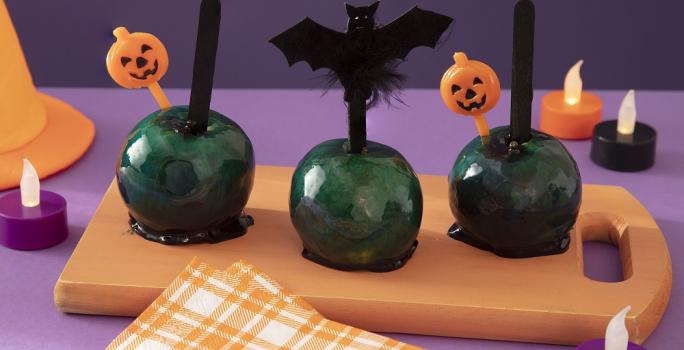 Foto da receita de maçã do amor da bruxa malvada servida em 3 porções sobre uma tábua de madeira com decoração de halloween em volta