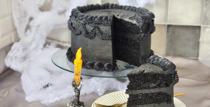 Foto da receita de Bolo de Veludo Preto. Observa-se um bolo alto preto decorado de preto, com uma decoração de Dia das Bruxas.