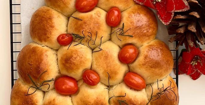Foto da receita de Pão Caseiro Natalino. Observa-se um pão assado e dourado em formato de árvore, decorado com tomatinhos cereja