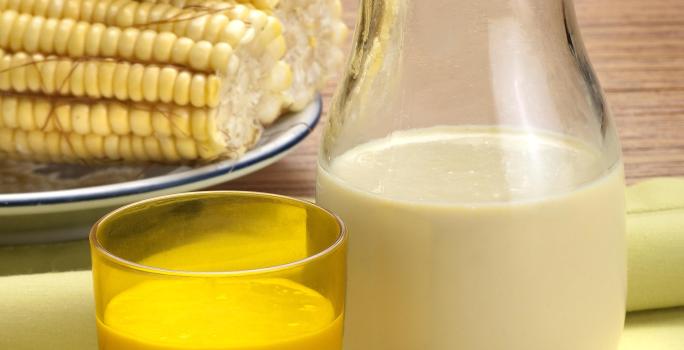 foto tirada de uma jarra com suco de milho e à frente um copo amarelo com a bebida