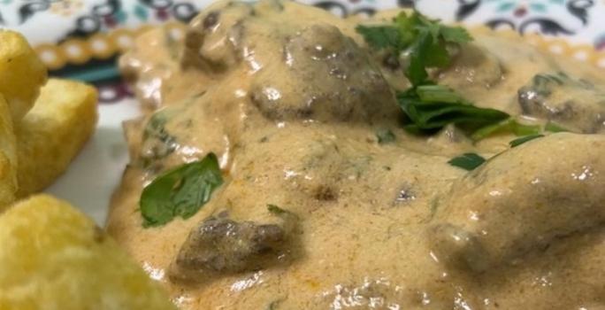 Foto da receita de Strogonoff de Carne. Observa-se um prato com o strogonoff cremoso e batatas fritas rústicas ao lado esquerdo.