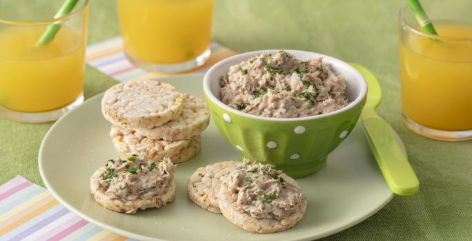 Foto da receita de Pate de Sardinha. Observa-se uma cumbuca verde clara com o patê dentro e, ao lado, biscoitos de arroz servidos com a receita.