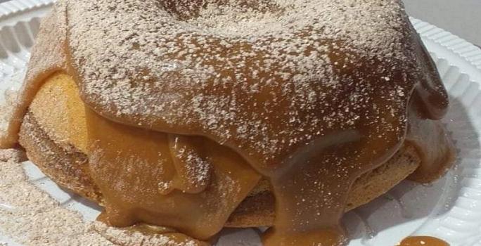 Foto em tons de marrom da receita de bolo vulcão de churros com bastante cobertura de doce de leite com canela salpicada por cima
