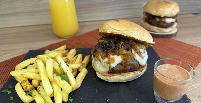 Fotografia de dois hambúrgueres acompanhados de uma porção de batatas fritas e um molho avermelhado.