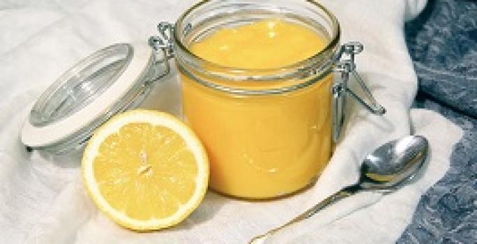 Foto da receita de Lemon Curd. Observa-se um potinho de vidro hermético com o creme de limão dentro e, ao lado esquerdo, um limão pela metade decora a foto.