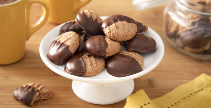 Foto da receita de Biscoitinho de Cappuccino. Observa-se uma boleira branca com 8 biscoitinhos em cima, banhados pela metade com chocolate.