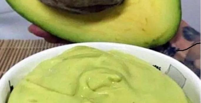 Foto da receita de Mousse de Abacate. Observa-se um potinho branco com a mousse cremosa dentro e um abacate pela metade atrás ilustrando.