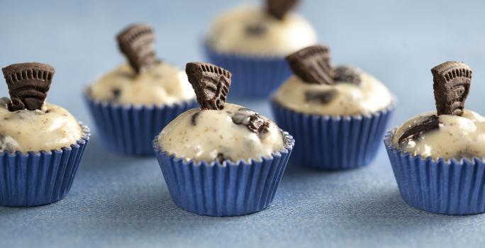 Fotografia em tons de azul e bege, mostrando seis docinhos decorados com pedaços de biscoito e tudo sobre bancada na cor azul.