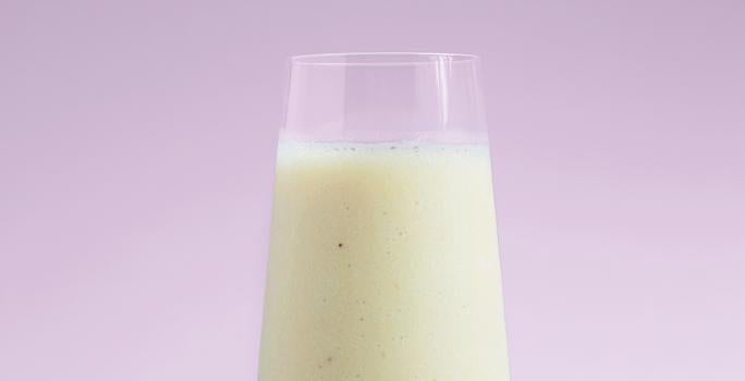 Fotografia em tons de lilás e branco e ao centro um copo transparente com leite.