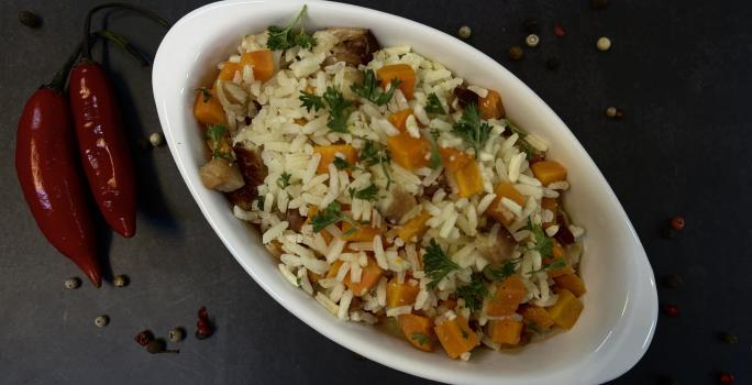 Foto vista de cima da receita de Arroz com Bacon e Cenoura, servido em um refratário de vidro branco, em uma bancada decorada com duas pimentas dedo-de-moça