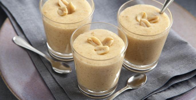 fotografia em tons de bege e cinza de uma bancada cinza vista de cima. Contém 3 copinhos com o creme de paçoca com amendoim por cima para decorar e abaixo um pano cinza.