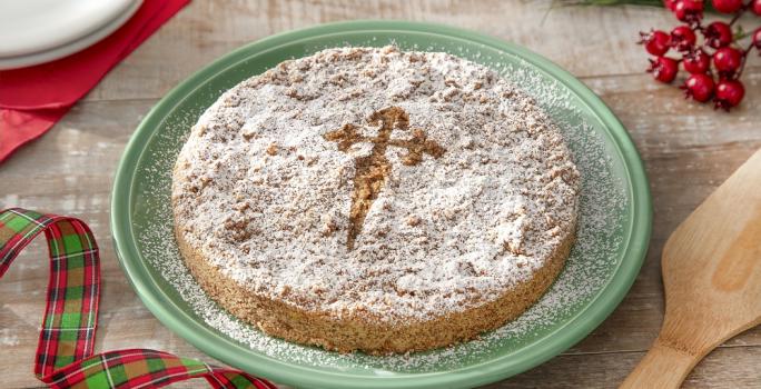 Foto da receita de torta de santiago servida em um prato verde grande sobre uma mesa de madeira com decoração de natal e uma espátula de madeira ao lado