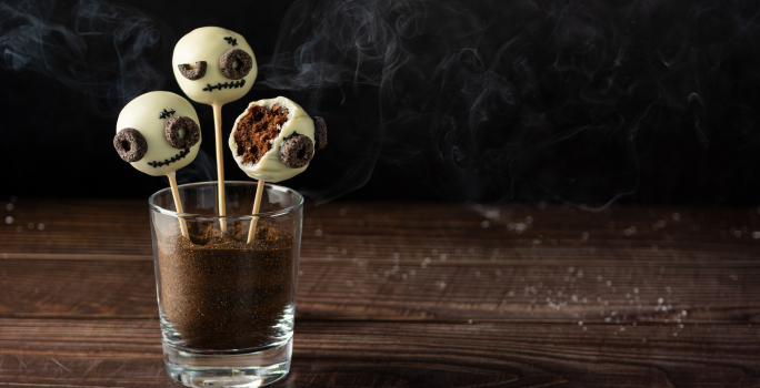 Fotografia de um bolo no palito coberto por chocolate branco, decorados com carinhas de monstro.