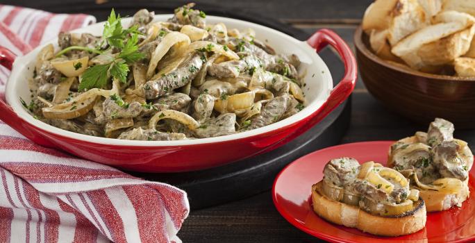 em uma mesa contém um pano listrado nas cores vermelho e branco, um prato cor vermelho com dois pães com aperitivo por cima e um recipiente com o aperitivo.