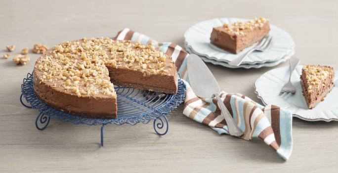 fotografia em tons de cinza e marrom de uma bancada cinza vista de cima. Contém dois pratos redondos e brancos com fatias de torta e garfos ao lado para servir. Um suporte para servir bolo azul contém a torta com fatias retiradas.