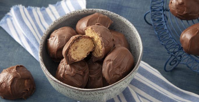 Foto da receita de Bombom de Farinha Láctea NESTLÉ Aveia. Observa-se um recipiente de cerâmica com 7 bombons dentro, sendo que o de cima está cortado ao meio e é possível ver o interior do bombom