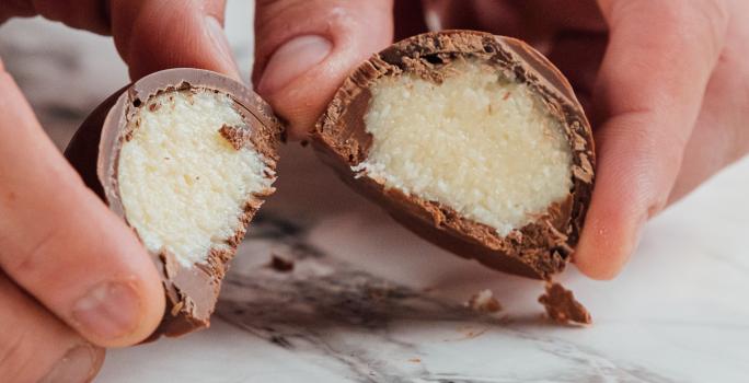 Foto da receita de Bombom de Prestígio. Observa-se uma foto bem perto do bombom cortado ao meio, expondo o recheio cremoso de coco.