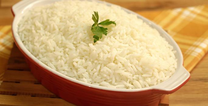 Foto de um recipiente vermelho com arroz branco dentro e uma folha de coentro decorando