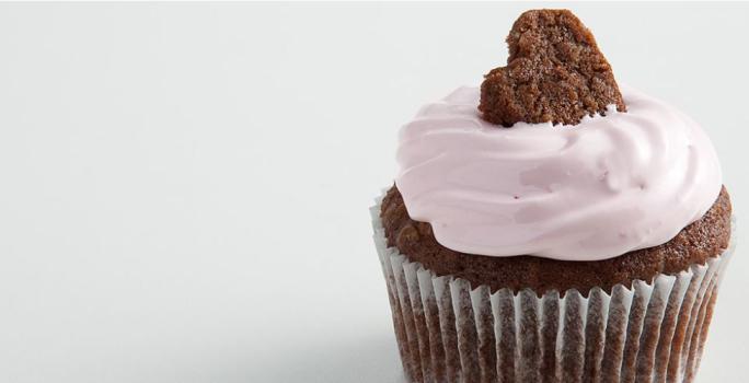 Fotografia em tons de branco, marrom e rosa vista de frente. Contém um bolinho de chocolate com creme de cereja e para decorar um mini bolinho em formato de coração por cima.