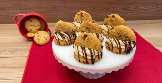 Fotografia mostra cookies cobertos por um creme branco e chocolate derretido, e meio cookie no topo.